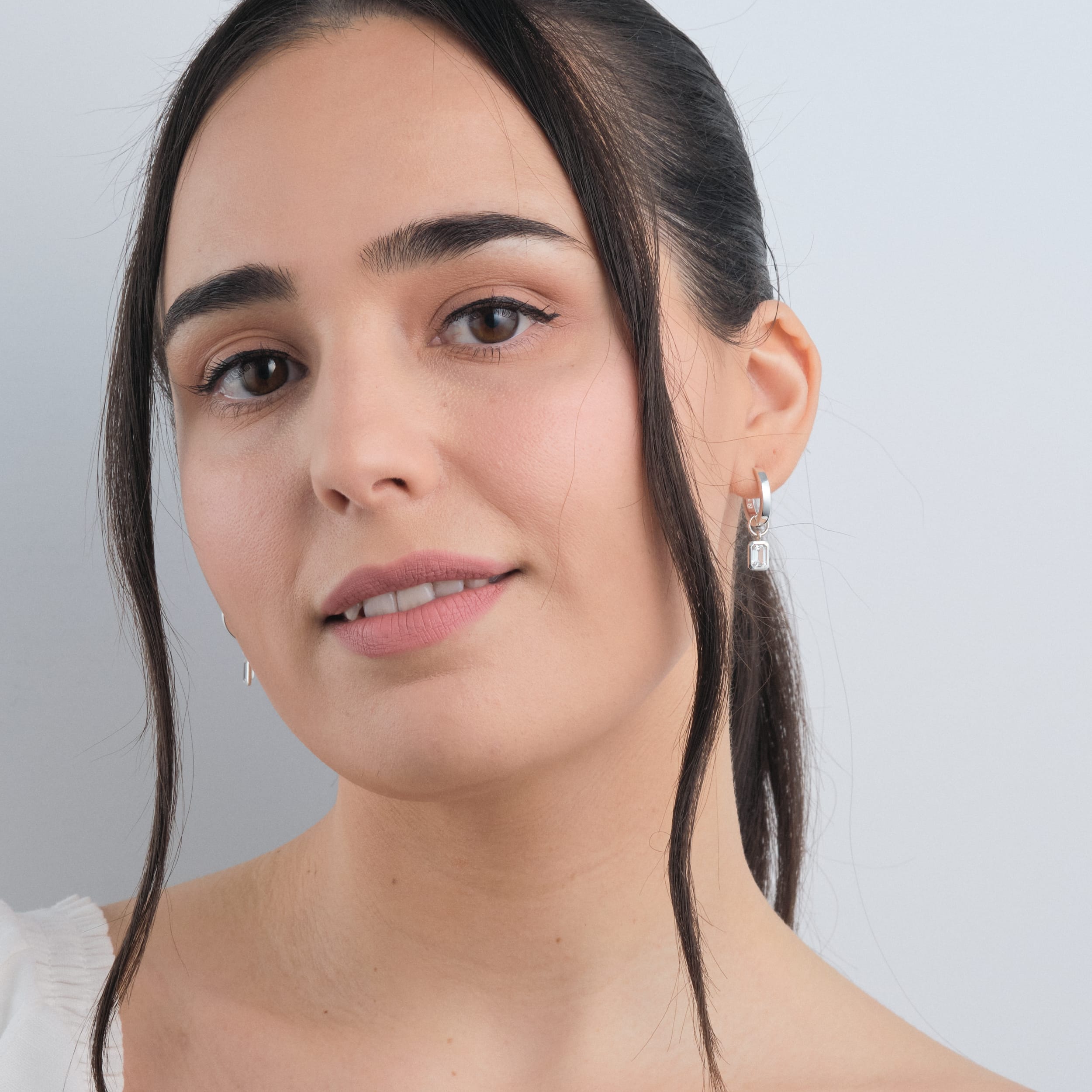 A woman wearing sterling silver huggie hoop earrings with interchangeable white topaz gemstone charms made with durable, irritation free sterling silver, these earrings are ideal for those seeking an affordable yet luxurious piece that can be styled for any occasion.