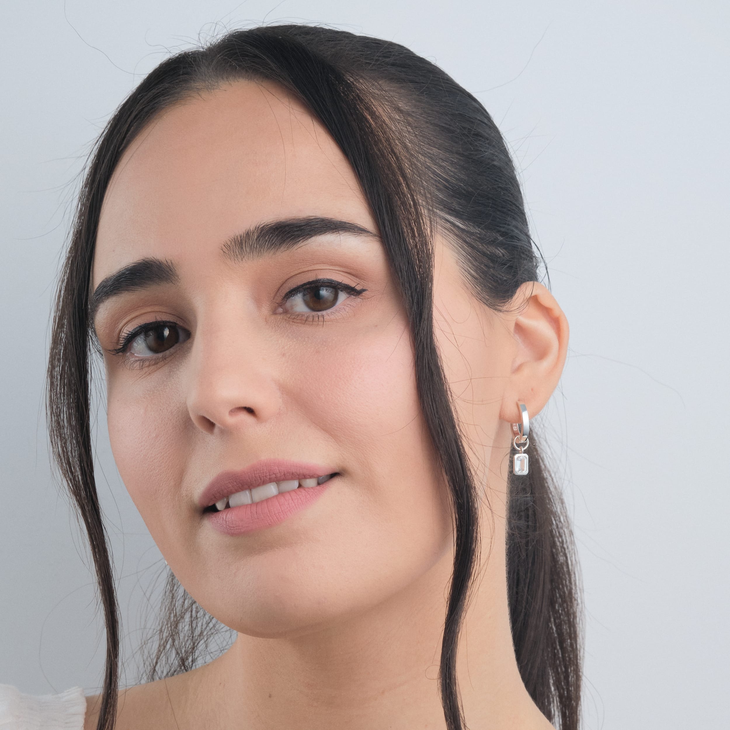 Front view of a woman wearing durable and irritation free huggie hoop earrings made from premium sterling silver with interchangeable white topaz gemstone charms. The perfect gift for customisable jewellery lovers.